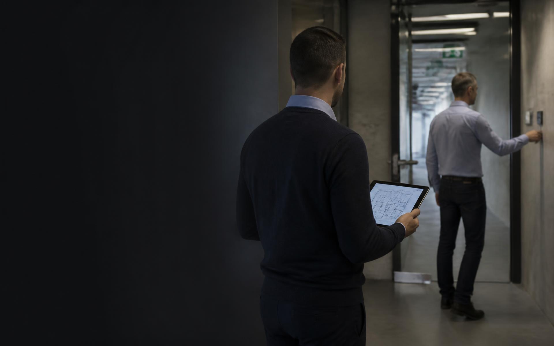 Bezpečnostní konzultanti procházejí moderní budovu s půdorysem objektu na tabletu